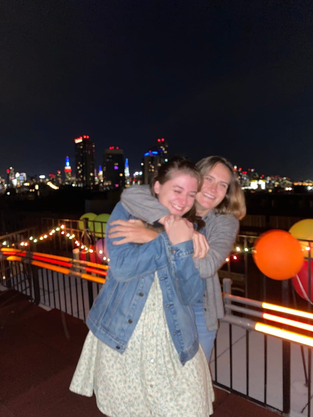 The two of us hugging on a rooftop at night, the Manhattan skyline lit up behind us